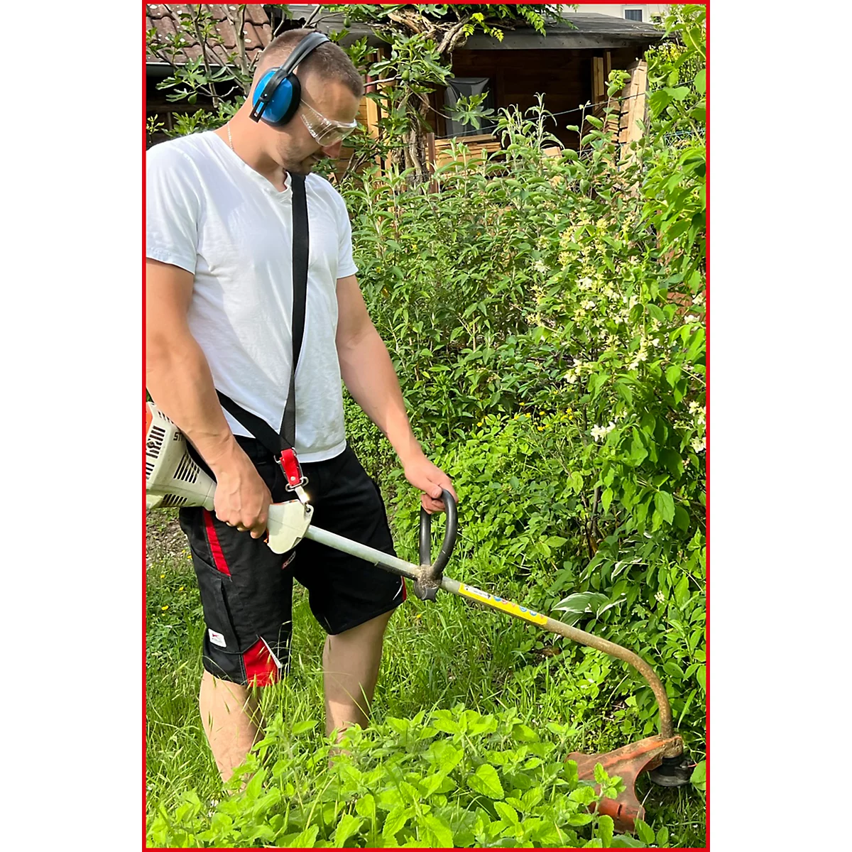 Ein Mann schneidet mit einem Rasentrimmer im Garten Gras. Er trägt Gehörschutz und Schutzbrille.